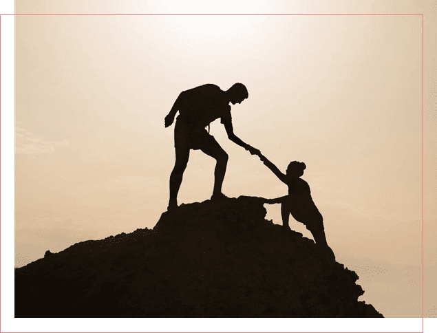 A man helping another person climb up the side of a hill.